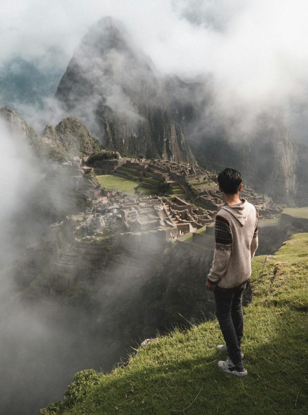 A man stands on a cliff edge overlooking the ancient ruins of Machu Picchu enveloped in mist.